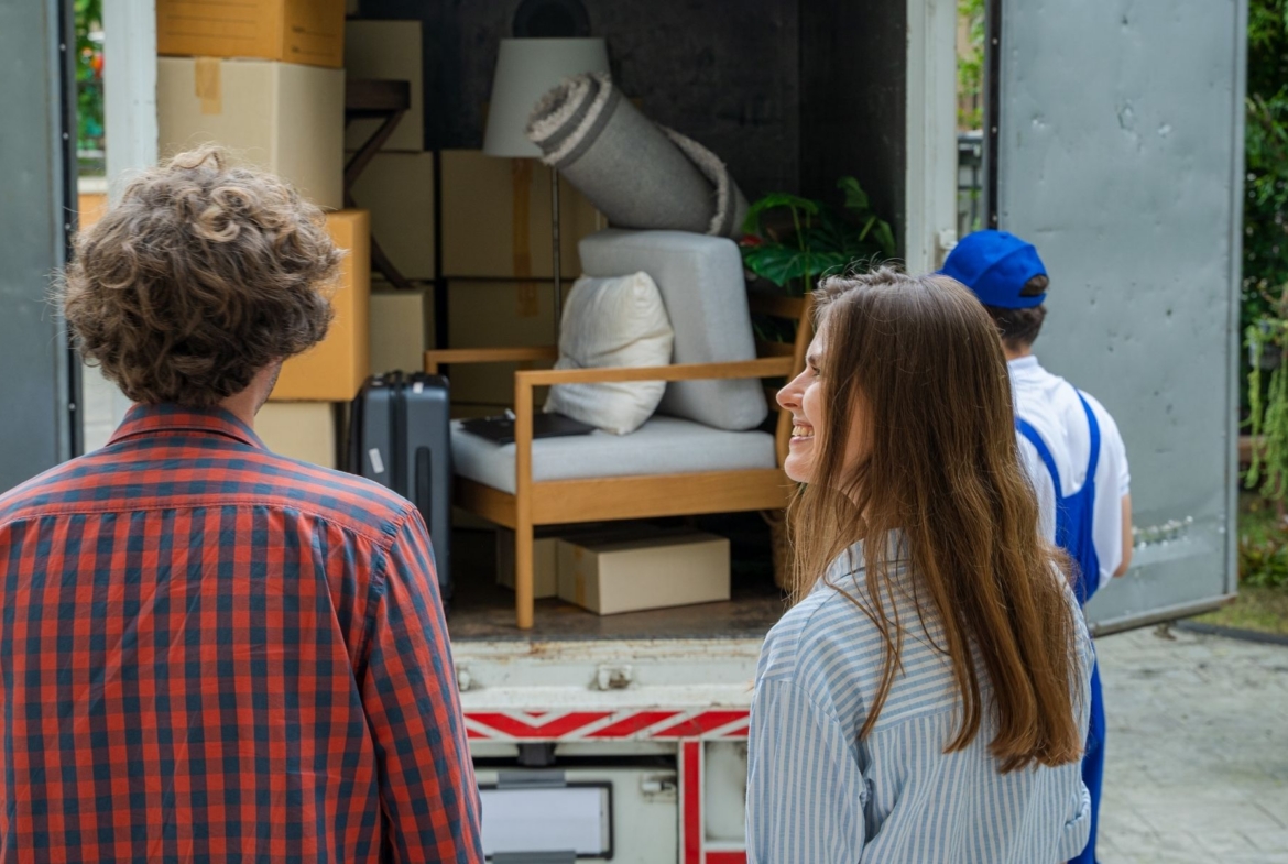 Couple standing beside movers loading furniture and boxes into a truck.