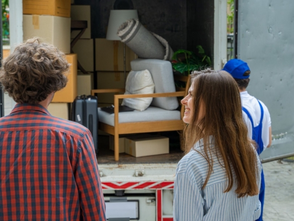 Couple standing beside movers loading furniture and boxes into a truck.