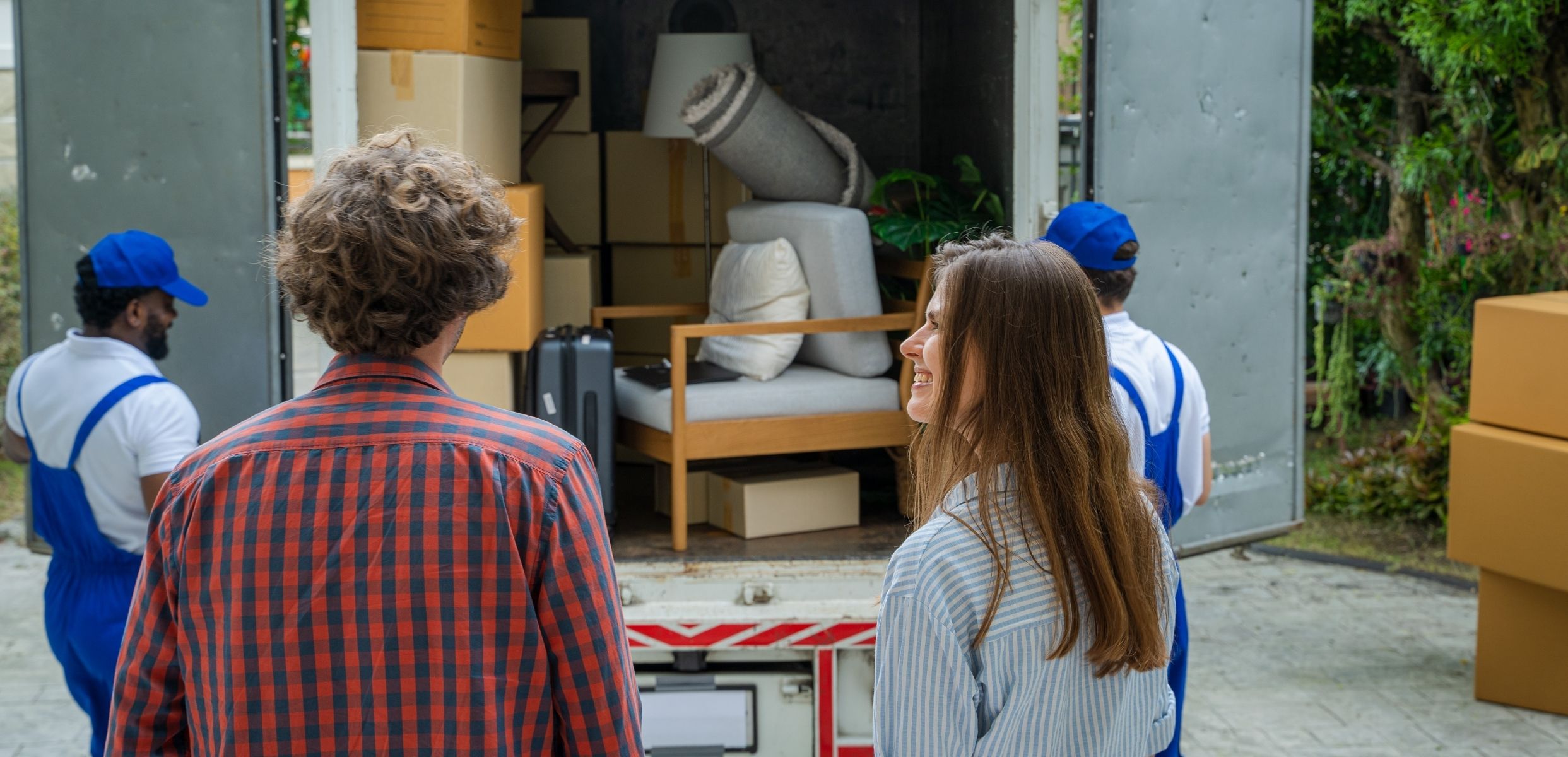 Couple standing beside movers loading furniture and boxes into a truck.
