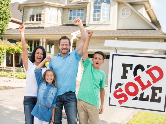 Family celebrating beside a sold sign in front of their new home